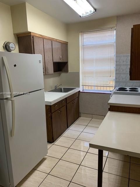 Kitchen featuring wood cabinetry, white laminate countertops, stainless steel sink, tiled flooring, and window with built-in blinds