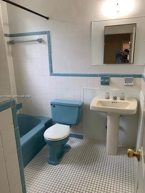 Full bathroom featuring white wall tile with blue accent trim, a pedestal sink, a blue soaking tub, and matching blue water closet