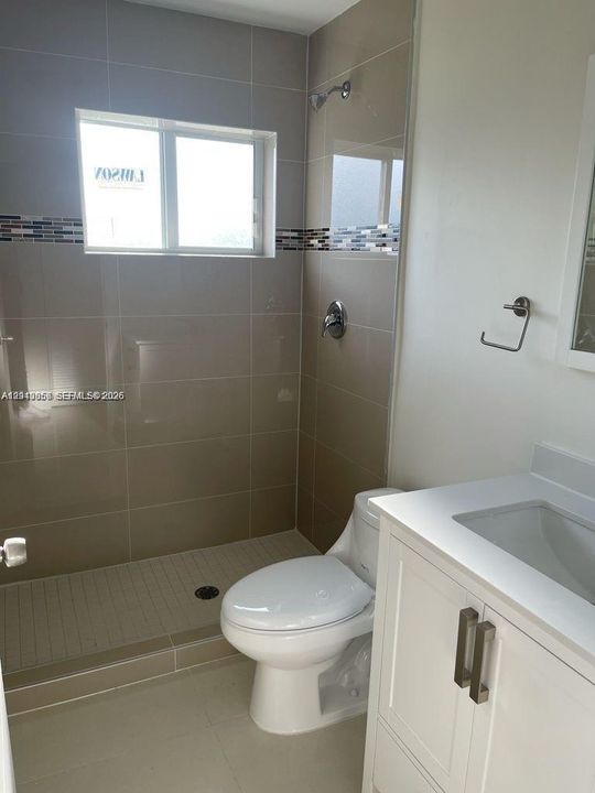Bathroom featuring a walk-in shower with large-format wall tile and decorative mosaic inlay, white vanity with integrated sink, and chrome fixtures