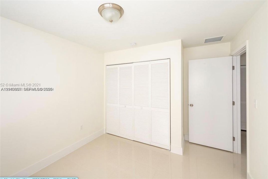 Neutral-toned room featuring large-format tile flooring, a four-panel louvered closet, a semi-flush mount ceiling fixture, and a solid-core interior door