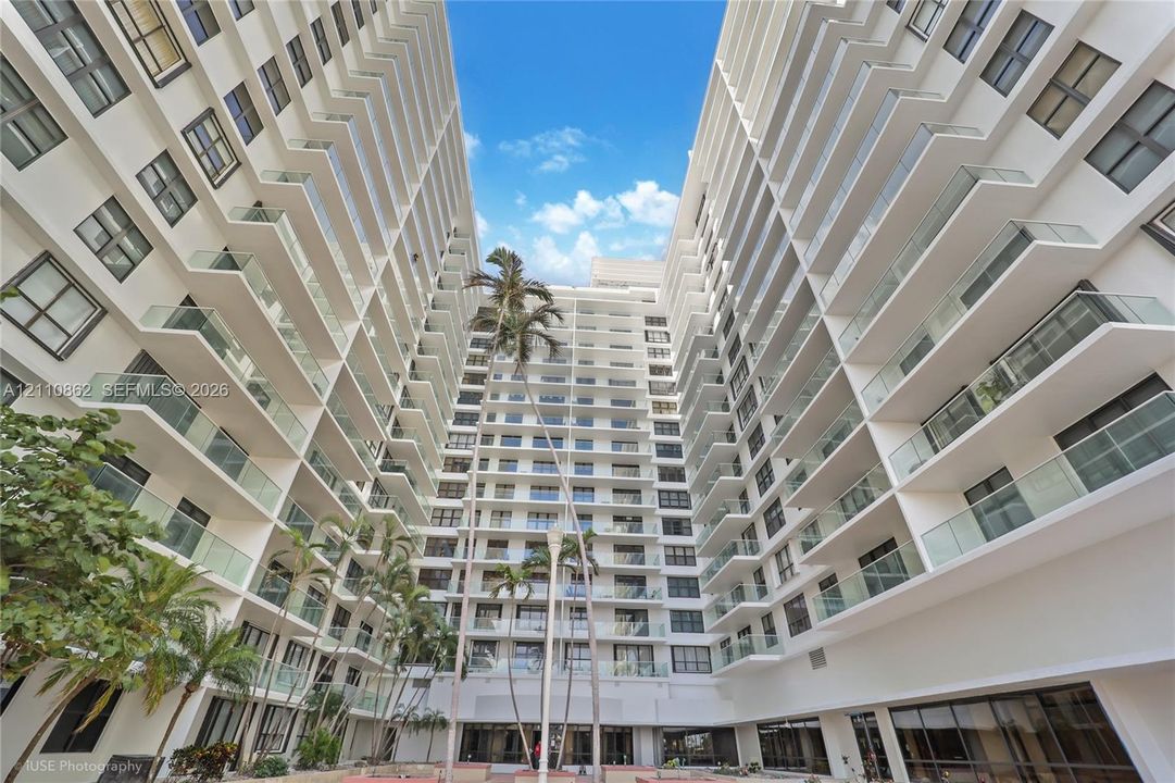 architecture featuring white structural siding, multiple stories of glass-railed balconies, and mature palm trees