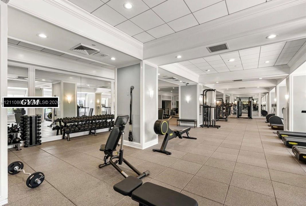 Fitness space featuring expansive wall mirrors, recessed ceiling lighting, crown molding, and tiled flooring