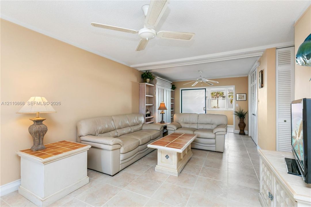 Neutral-toned tile flooring, dual ceiling fans, built-in shelving unit, and louvered closet doors