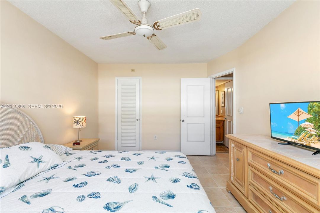 Interior room featuring neutral wall tones, large-format tile flooring, a white paneled door, a white louvered-style closet door, and a ceiling fan with integrated lighting