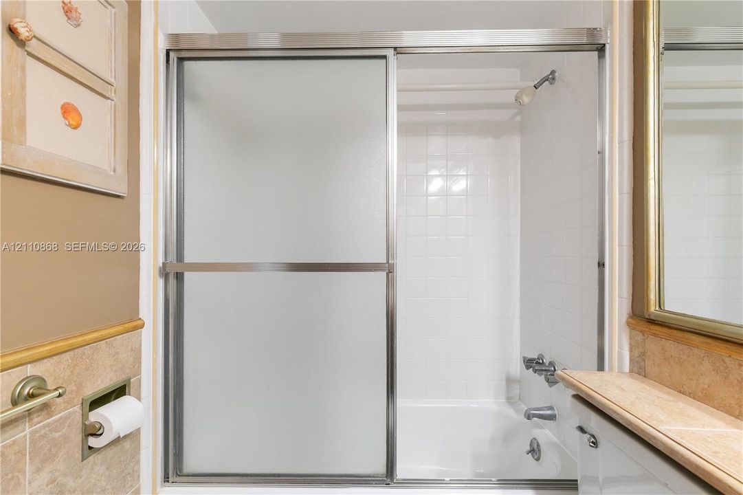 Shower with sliding frosted glass doors, white tile surround, metal shower head and faucet hardware, and light-toned tile wainscoting
