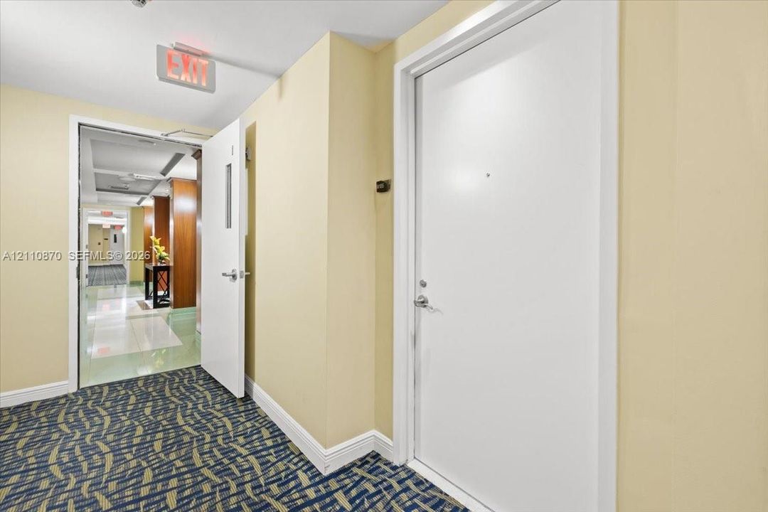 Interior hallway featuring patterned carpeting, neutral wall paint, and white solid-core doors with metallic hardware