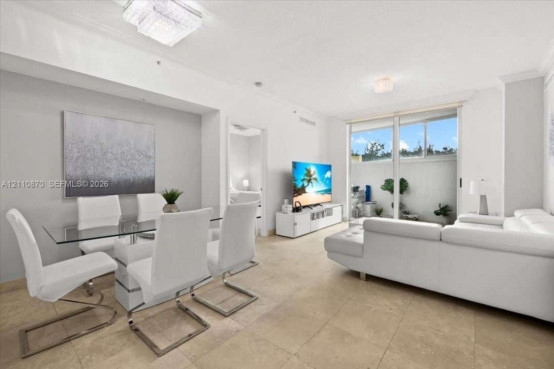 Open-concept living space featuring large-format tile flooring, crown molding, dual flush-mount ceiling light fixtures, and expansive sliding glass doors