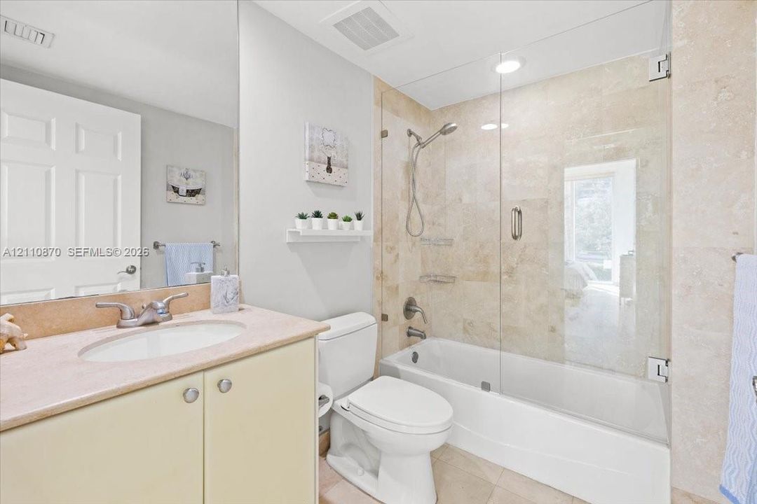 Full-height vanity cabinet with a stone countertop, recessed oval sink, stone-tiled shower surround, and a frameless glass tub enclosure