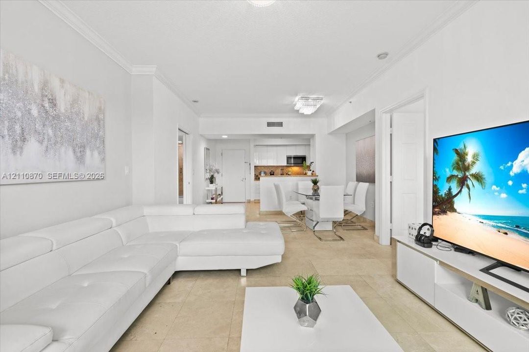 Open-concept interior featuring light-toned tile flooring, crown molding, a kitchen breakfast bar, and recessed lighting