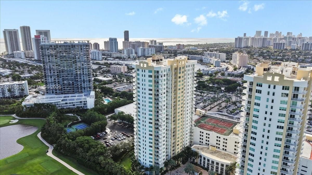High-rise residential tower featuring wraparound balconies, multi-story glass-paned windows, tennis courts, and proximity to an expansive golf course