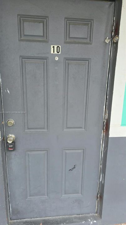 Gray six-panel entry door with integrated peephole, numerical signage, and metallic hardware