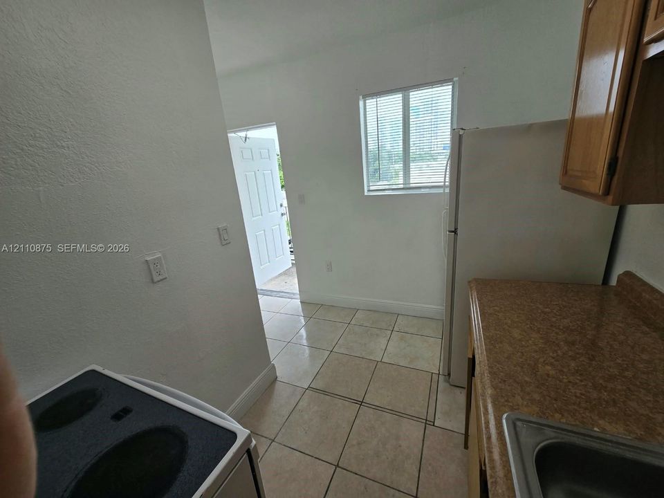 Kitchen featuring tile flooring, wood-finish cabinetry, a white refrigerator, an electric range, and a single-pane window