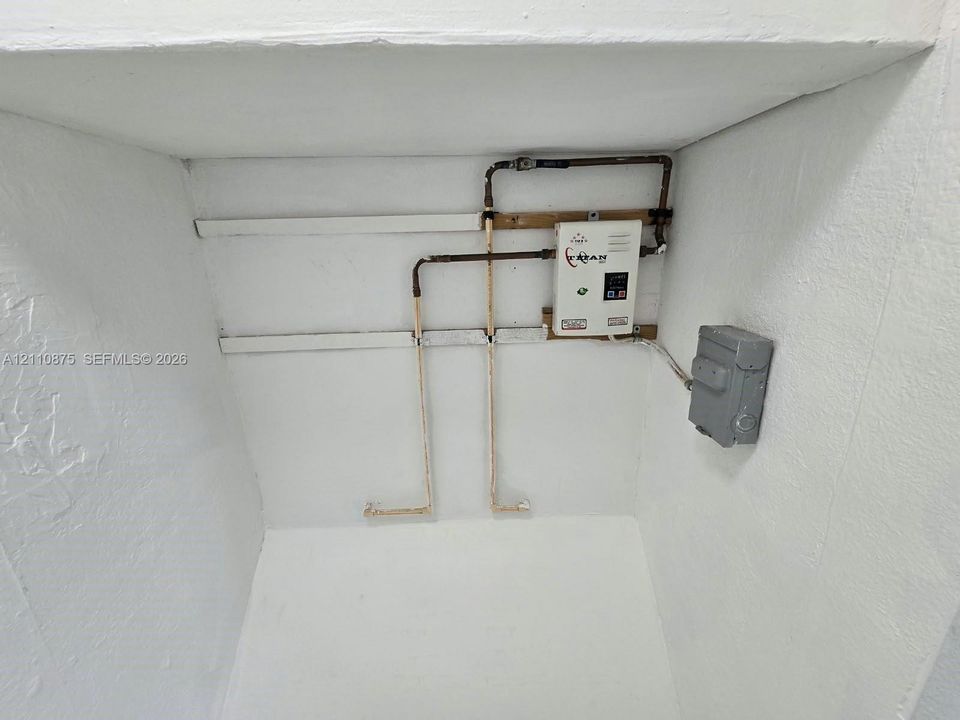Tankless electric water heater featuring copper plumbing connections and a wall-mounted electrical disconnect switch