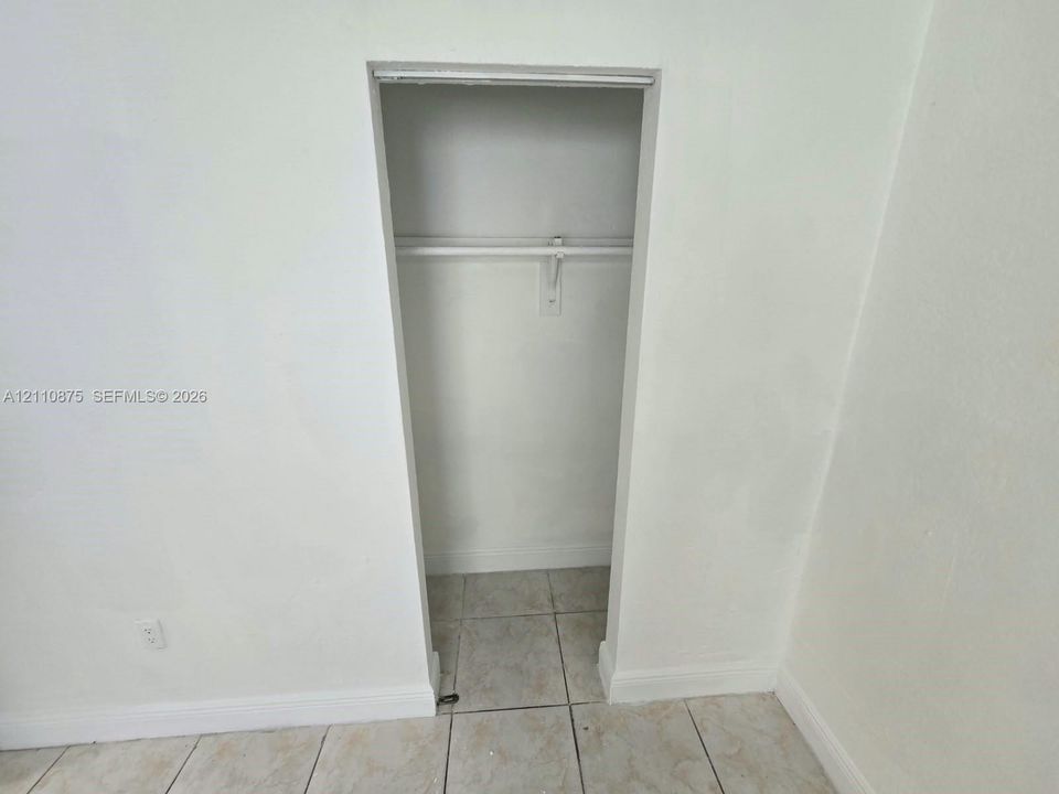 Built-in closet featuring a horizontal hanging rod and ceramic tile flooring