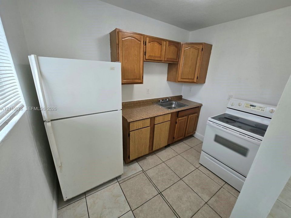 Kitchen area featuring wood cabinetry, stone-finish countertops, stainless steel sink, tiled flooring, and white kitchen appliances