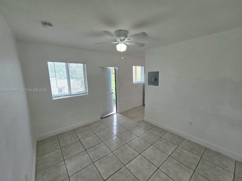 Interior space featuring neutral wall tones, large-format ceramic tile flooring, a ceiling-mounted fan with integrated lighting, and multiple windows providing natural illumination