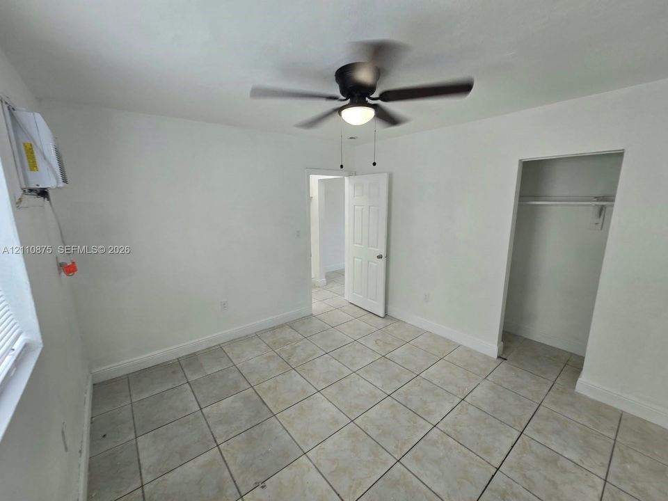 Room featuring neutral-toned tile flooring, a multi-blade ceiling fan with integrated lighting, and an inset closet with a built-in hanging rod
