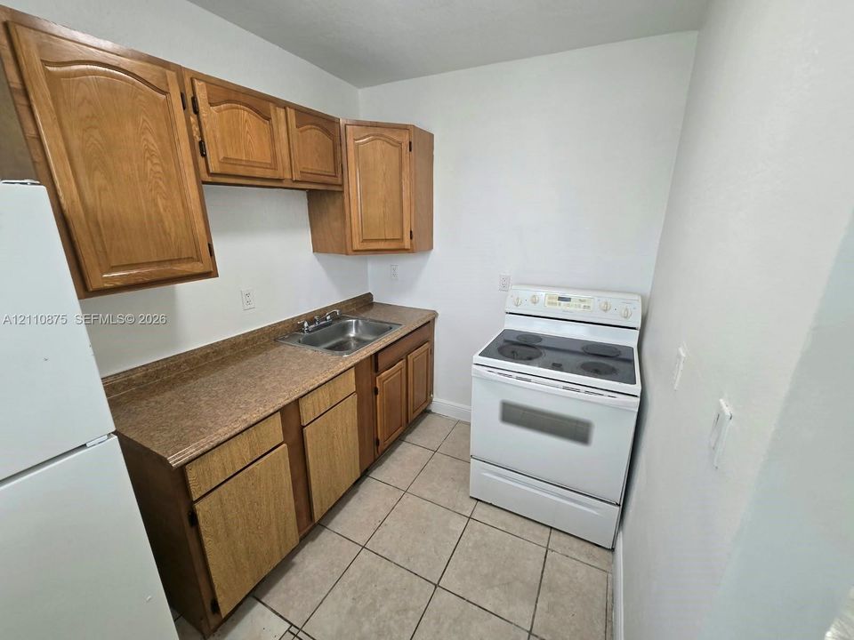 Kitchen featuring wooden cabinetry, laminate countertops, a double-basin stainless steel sink, a white electric range, and tile flooring