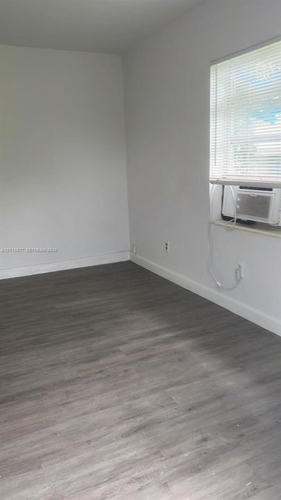 Neutral wall tones, wood-finish flooring, window with integrated blinds, and built-in wall-mounted air conditioning unit