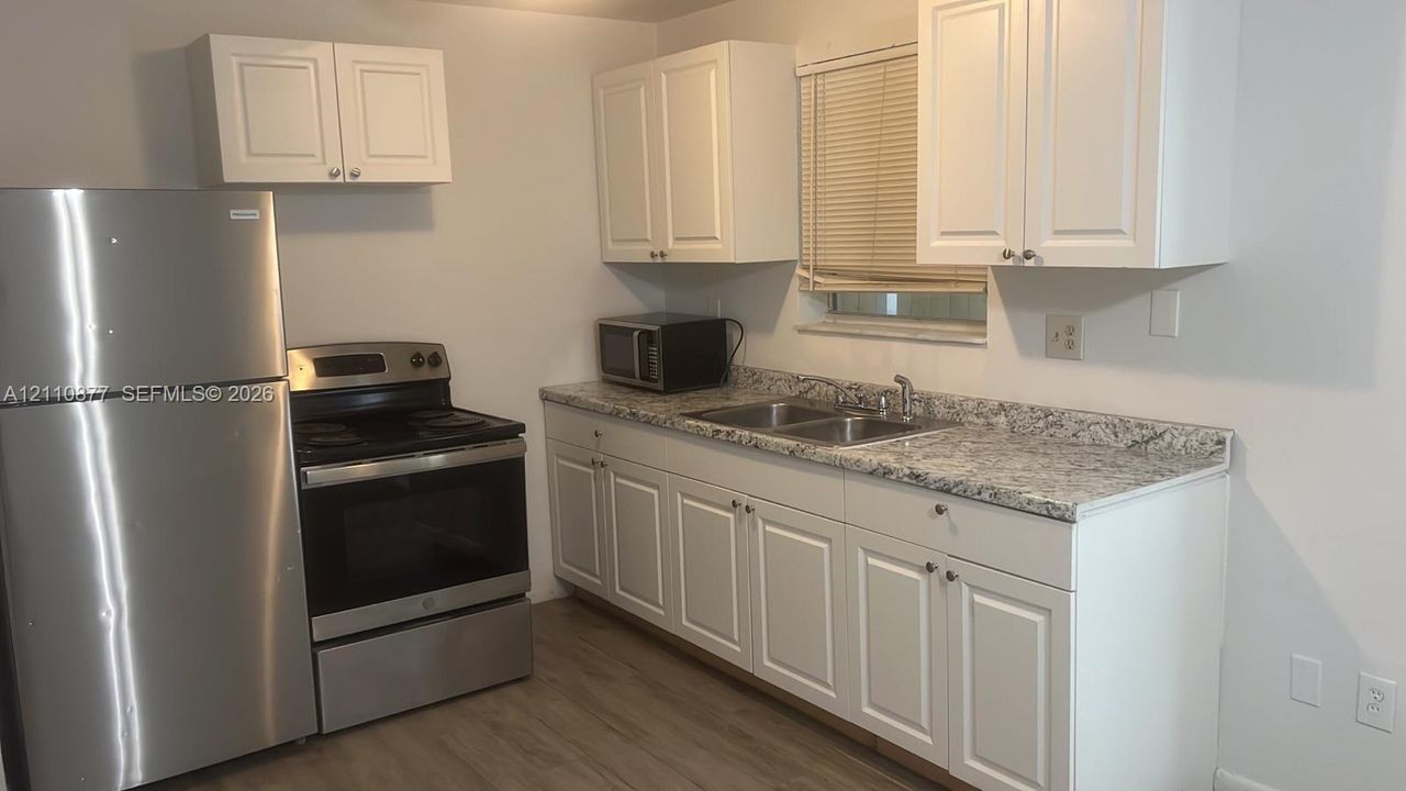 Kitchen featuring white shaker-style cabinetry, patterned stone-finish countertops, dual-basin stainless steel sink, and stainless steel appliances