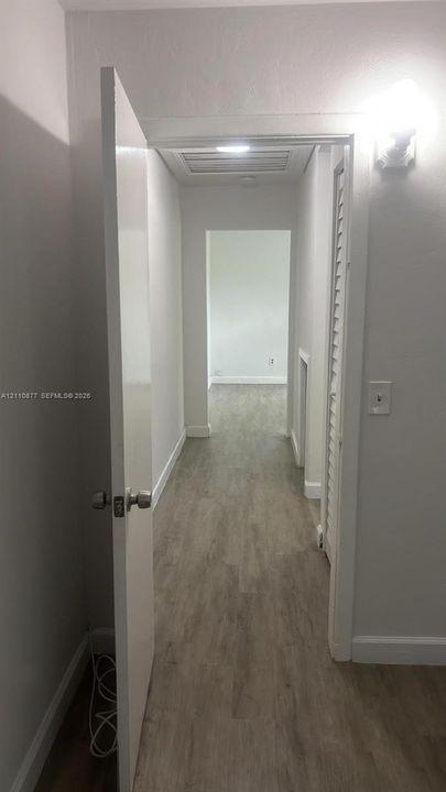 Hallway featuring wood-finish flooring, ceiling-mounted lighting, and a louvered closet door