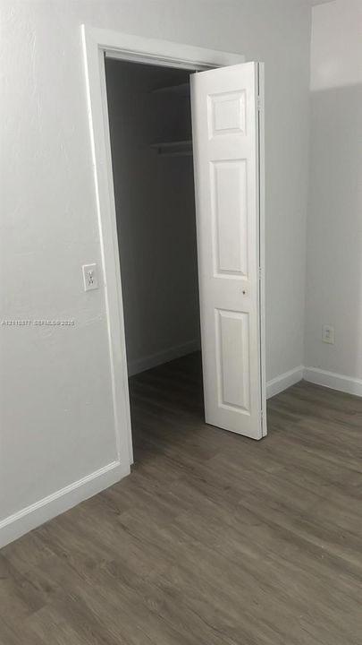 Wood-finish flooring, neutral wall tones, and a closet featuring a three-panel door with interior shelving