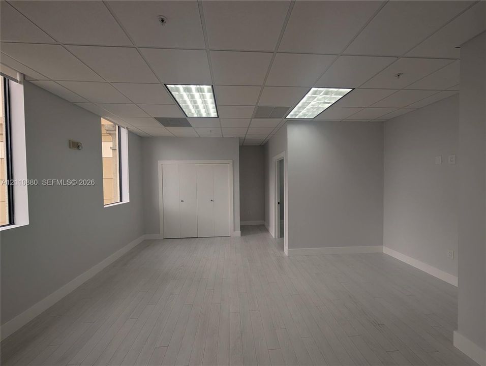 Open workspace featuring wood-finish flooring, recessed fluorescent lighting, drop ceiling panels, and double-door closet storage
