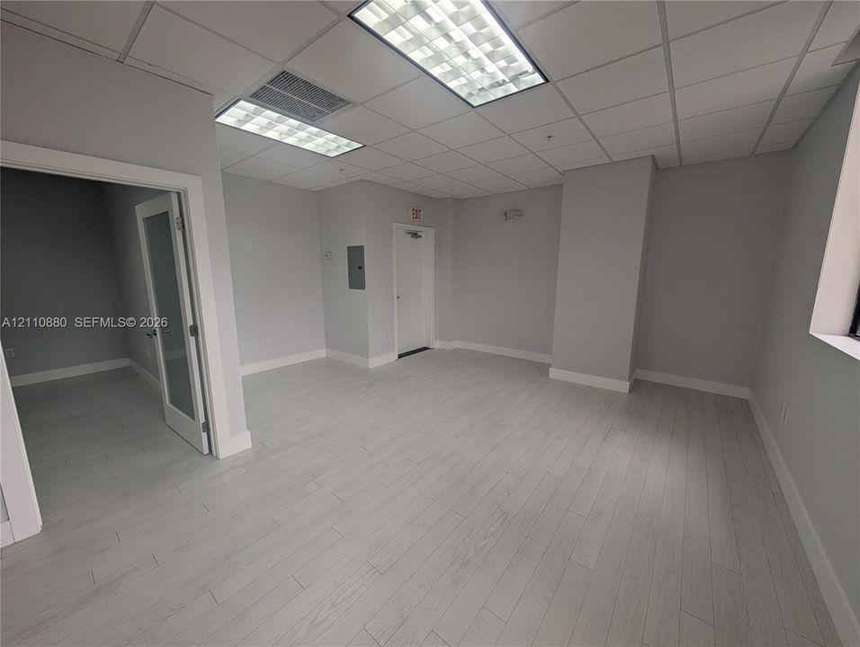 Interior space featuring wood-finish flooring, suspended acoustic ceiling tiles, recessed fluorescent lighting, and a glass-paneled door