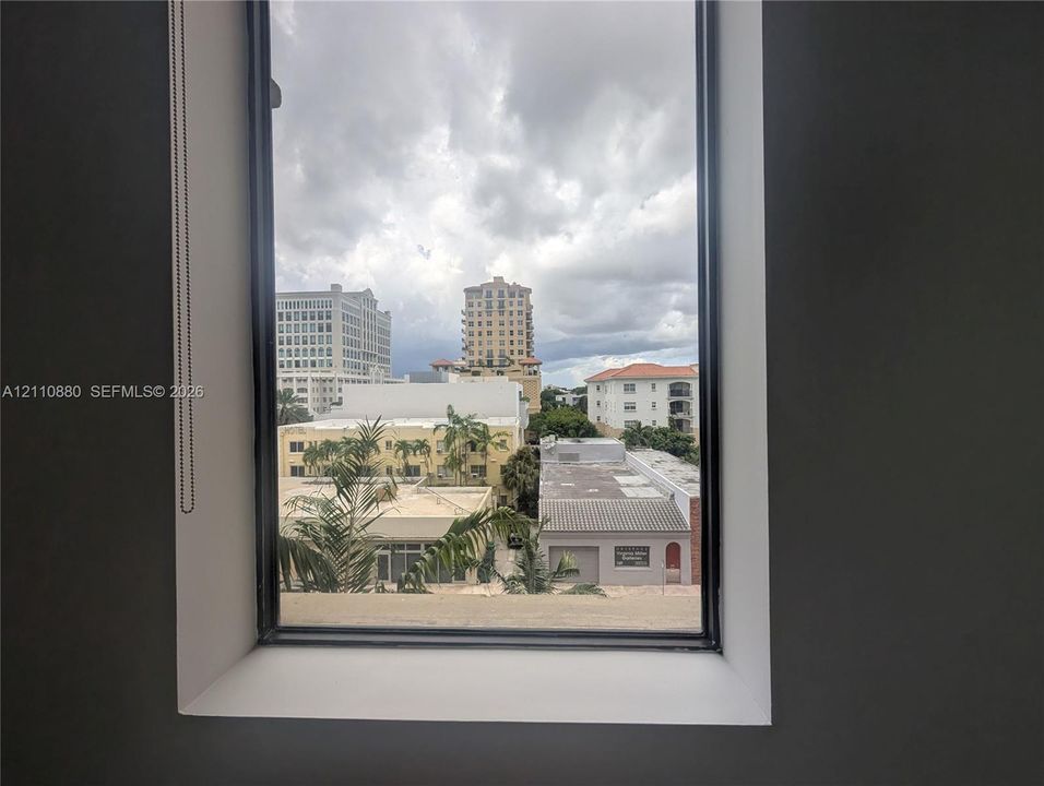 Floor-to-ceiling window with a black metal frame, integrated retractable shade, and urban cityscape backdrop