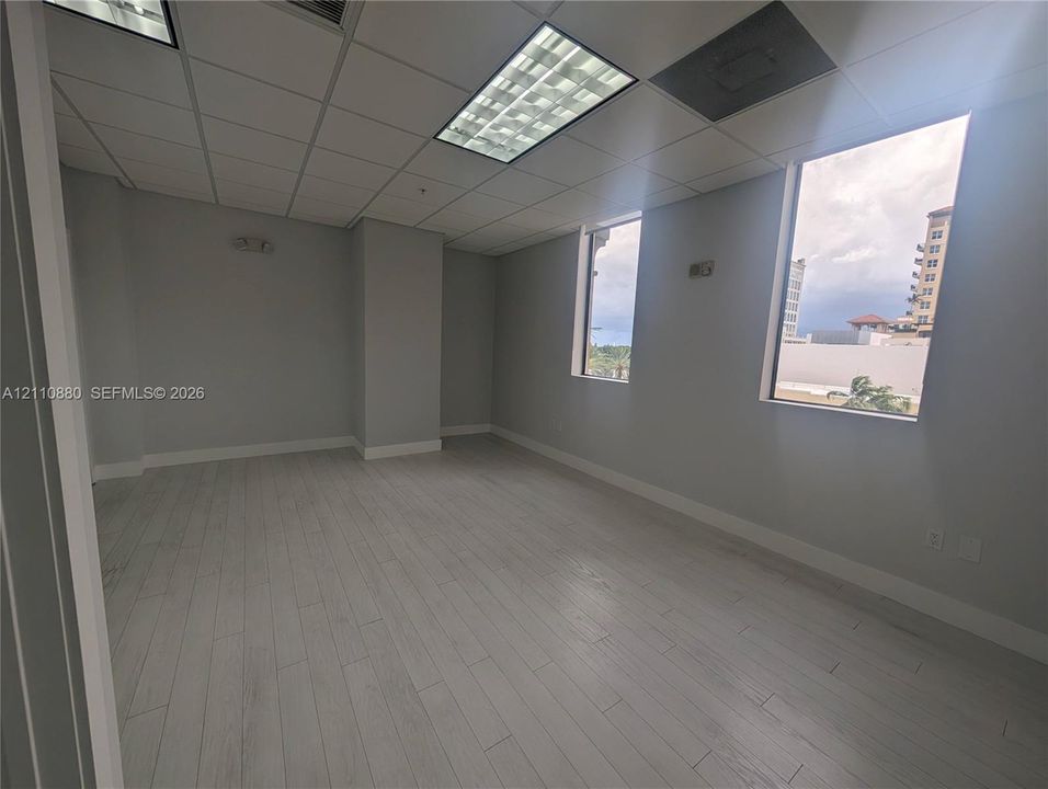 Open interior space featuring light-toned wood-finish flooring, neutral walls, recessed drop ceiling lighting, and tall vertical windows