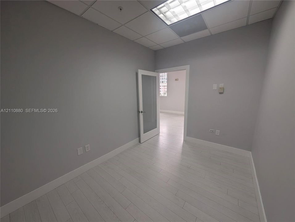 Interior room featuring wood-finish flooring, drop ceiling with recessed lighting, and a single-panel door with an integrated frosted glass pane