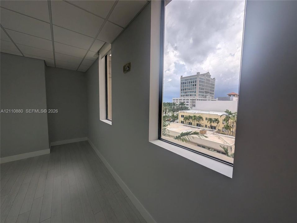 Interior space featuring wood-finish flooring, drop ceiling panels, neutral wall paint, and large windows with exterior urban scenery
