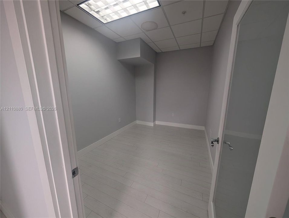 Interior space featuring wood-finish flooring, a glass-panel door with a brushed-metal lever handle, and a recessed ceiling grid with integrated lighting
