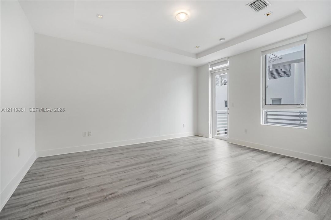 Neutral-toned room featuring wood-finish flooring, recessed ceiling lighting, a tray ceiling, and a full-height glass door