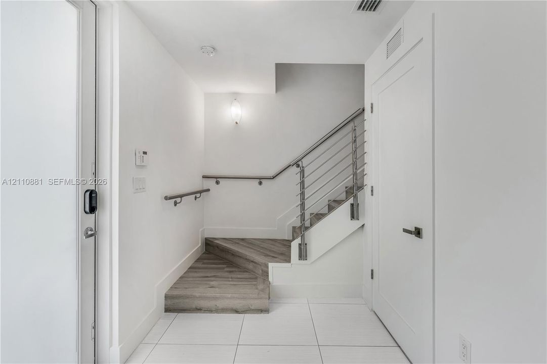 Entryway featuring large-format white tile flooring, wood-finish stair treads, and a custom staircase with stainless steel cable railings and wall-mounted handrails