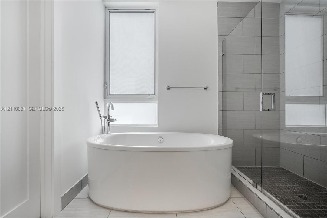 Freestanding oval soaking tub with chrome fixtures, glass-enclosed shower with horizontal wall tile, and large-format floor tile
