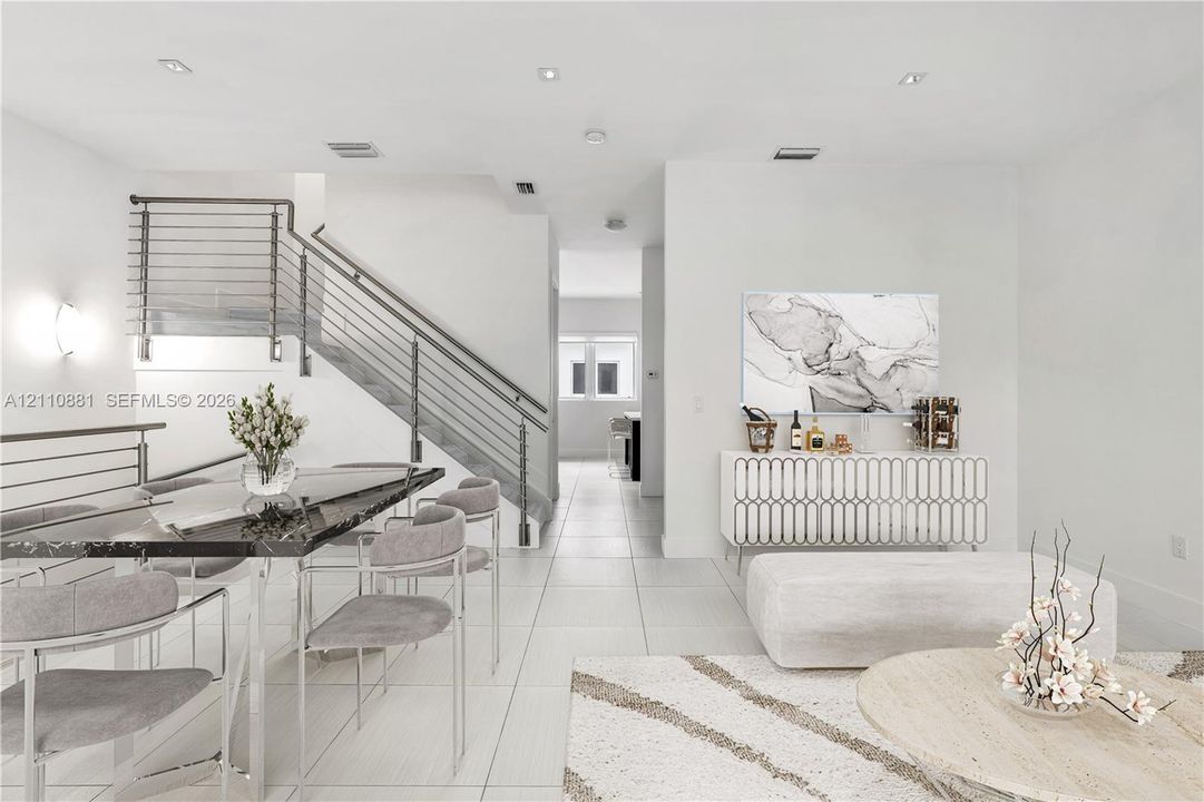 Open-concept interior with neutral tile flooring, staircase featuring horizontal metal railings, and recessed ceiling lighting
