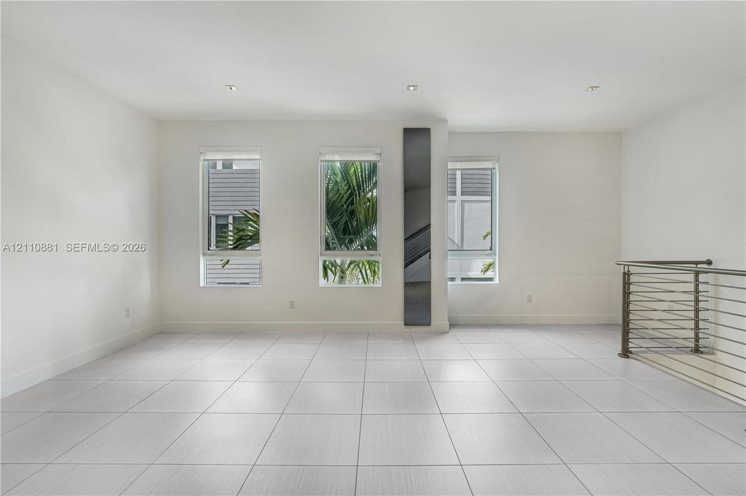 Open-concept interior featuring large-format tile flooring, recessed lighting, vertical paneled accent wall, and horizontal metal railing
