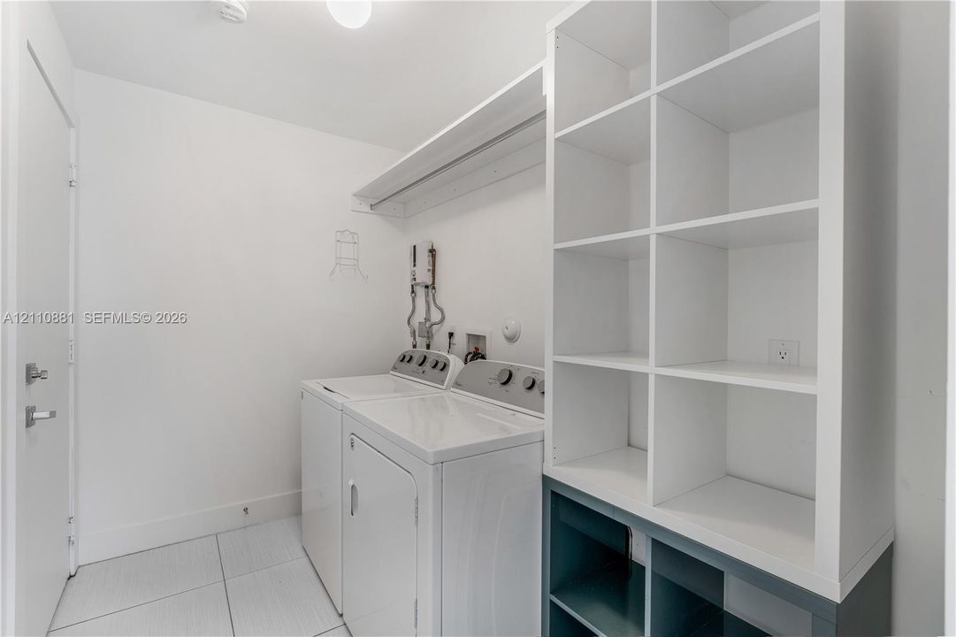 Laundry space featuring large-format tile flooring, white built-in shelving, and an integrated overhead hanging rod