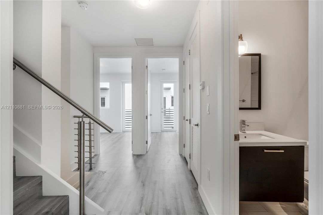 Hallway featuring wood-finish flooring, staircase with metal horizontal-bar railing, and built-in vanity with a rectangular sink and white countertop