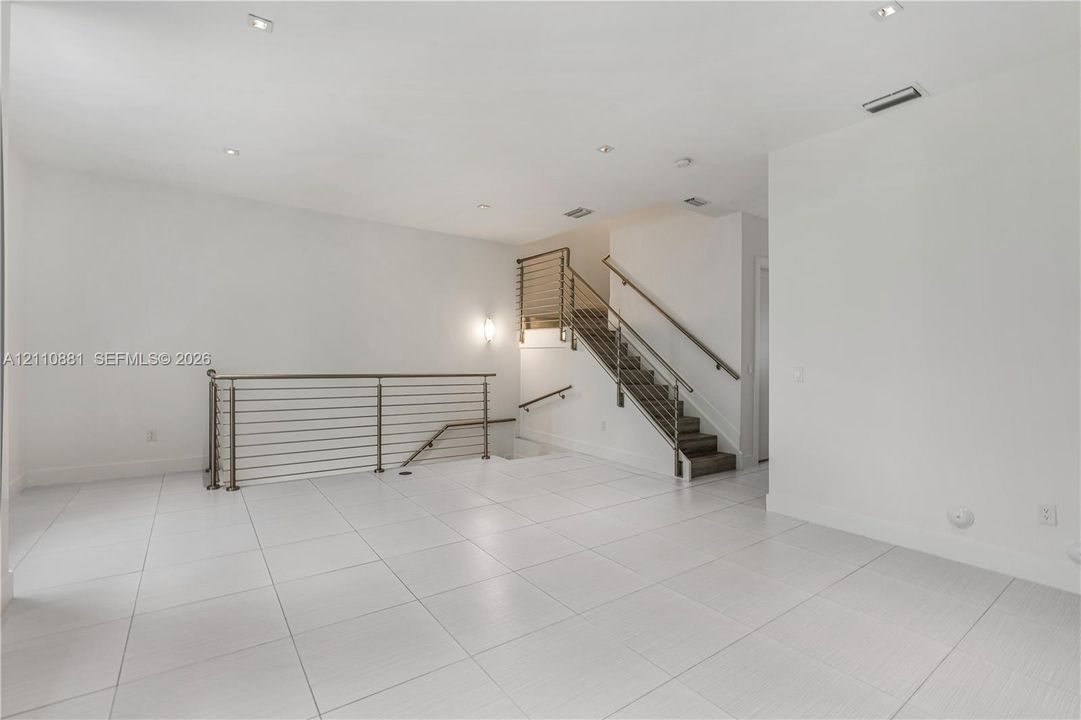 Large-format light-toned tile flooring, recessed ceiling lighting, and staircase featuring a metal horizontal bar railing system