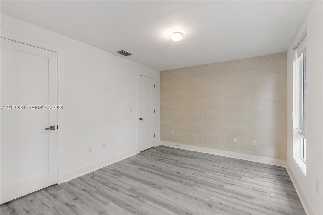 Neutral interior space featuring wood-finish flooring, a textured accent wall, two panel doors with metallic hardware, and a single vertical window