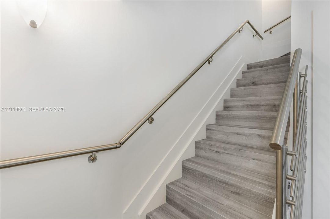 Staircase featuring wood-finish treads, wall-mounted metal handrails, and a matching metal vertical balustrade