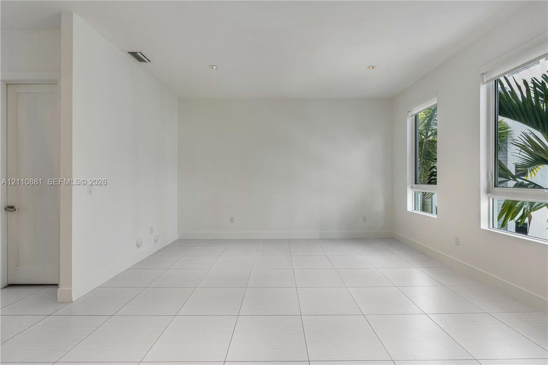 Interior space featuring large-format ceramic tile flooring, neutral white walls, recessed ceiling lighting, and multiple windows with white frames