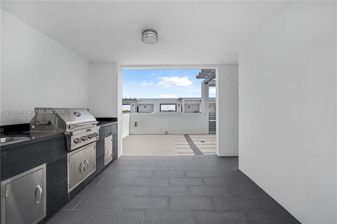 Outdoor kitchen featuring a built-in stainless steel grill, stone countertop, stainless steel cabinetry, and large-format tile flooring