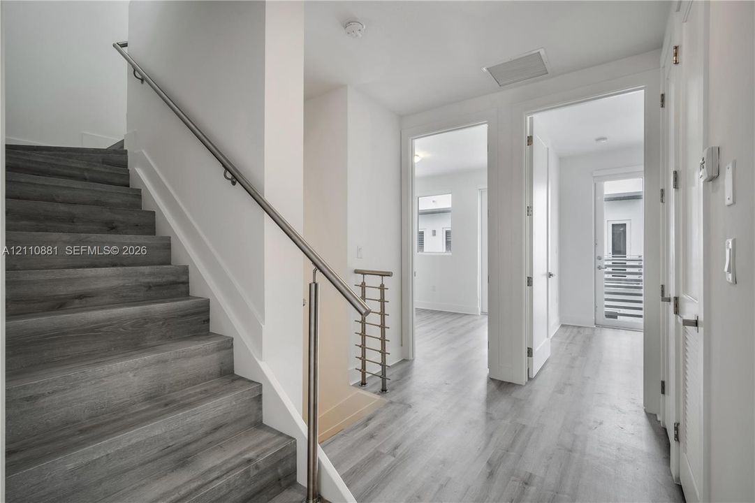Staircase featuring wood-finish treads and metal handrails, complemented by wood-finish flooring, neutral wall finishes, and a glass-paneled exterior door