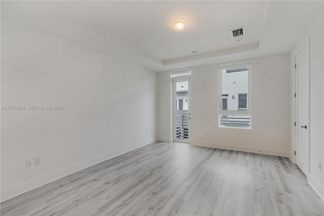 Interior room featuring neutral wall paint, wood-finish flooring, tray ceiling with recessed lighting, and a glass-paneled door