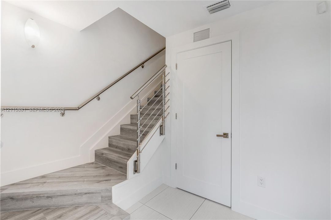 Staircase featuring wood-finish treads, a horizontal stainless steel cable railing system, and a wall-mounted metal handrail