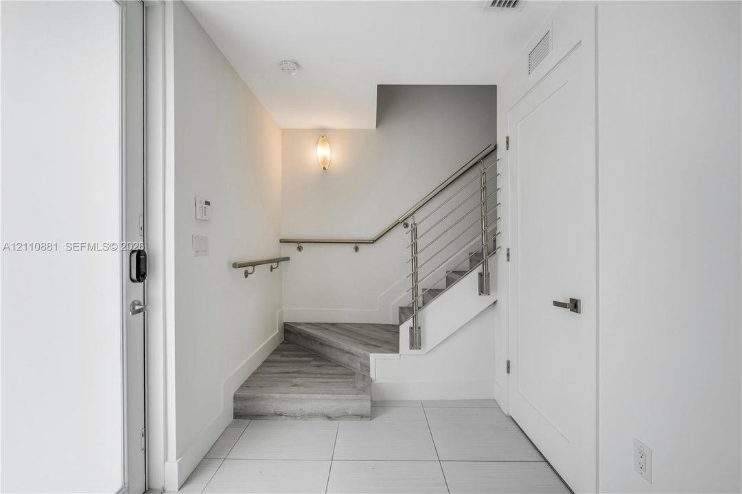 Entryway featuring large-format tile flooring, a wood-finish staircase, and a metal cable railing system with a wall-mounted handrail