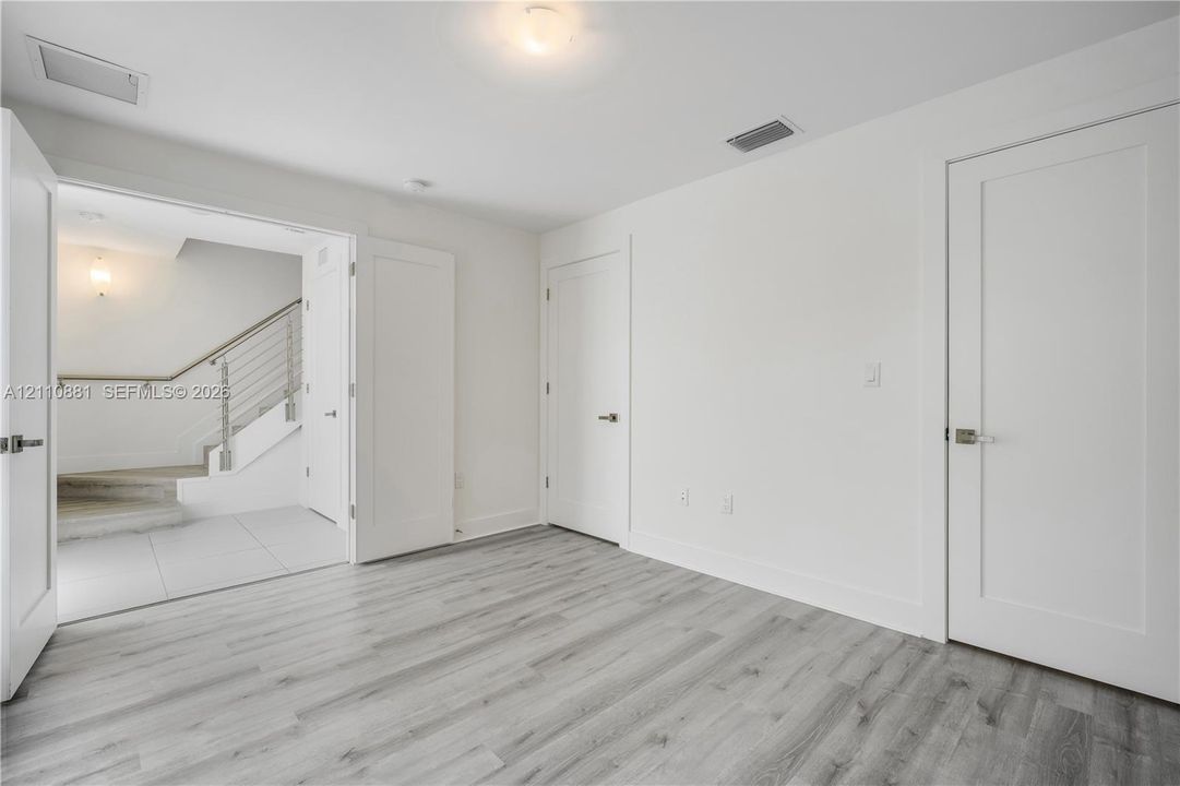 Interior space featuring wood-finish flooring, white walls, and three-panel interior doors with brushed nickel hardware